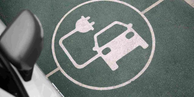 Símbolo de coche eléctrico con enchufe sobre asfalto
